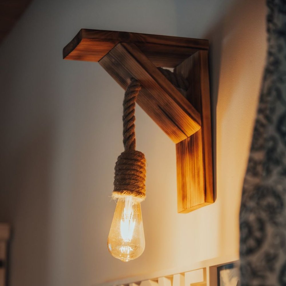 Rustykalna lampa na sznurze z żarówką w stylu industrialnym na tle drewnianej belki