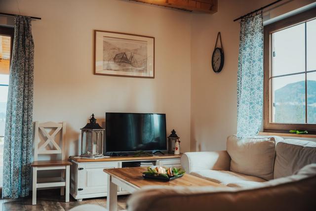 Salon z telewizorem na białej komodzie, kanapą i oknem z widokiem na góry