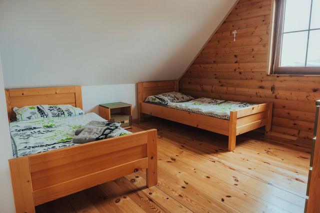 Poddaszowa sypialnia z dwoma pojedynczymi łóżkami, drewnianą podłogą i oknem w skosie
